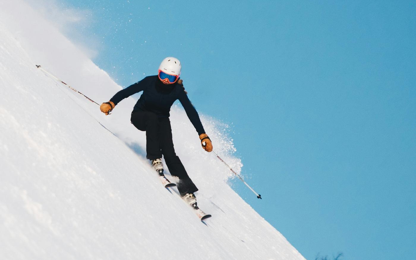 A skier carving down an open powder face under blue sky