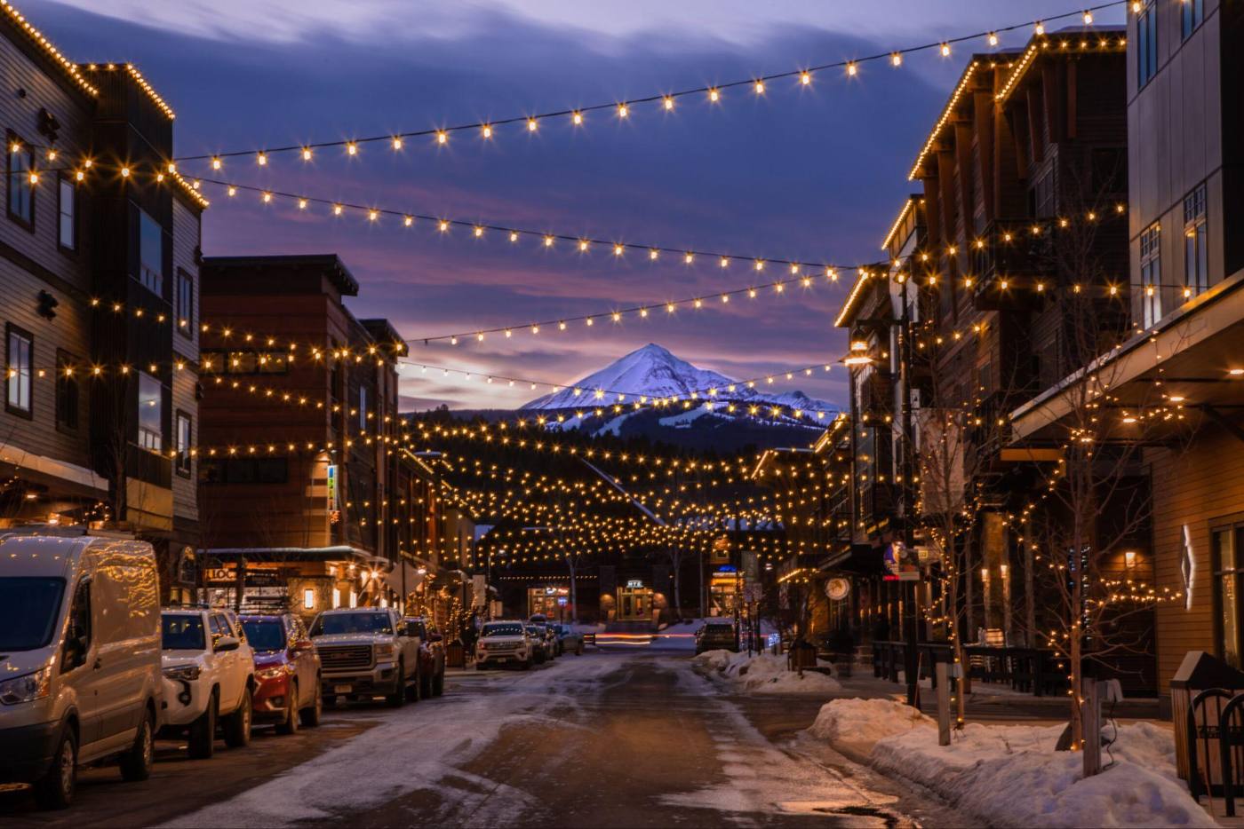 Big Sky Town Center at dusk under string lights, with Lone Peak beyond
